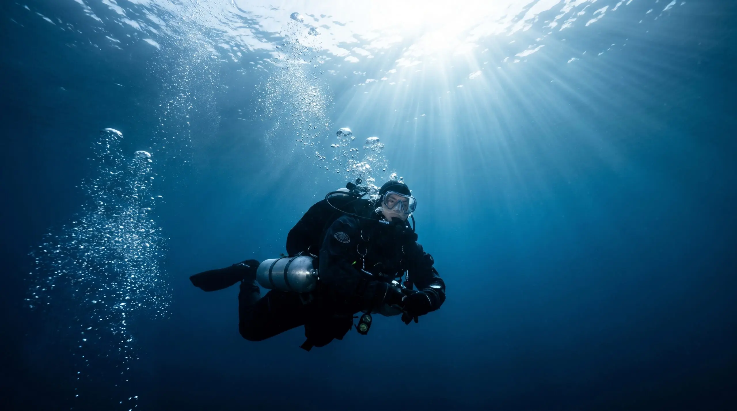 A scuba diver ascending slowly toward the sunlit surface, the careful ascent that helps prevent decompression sickness