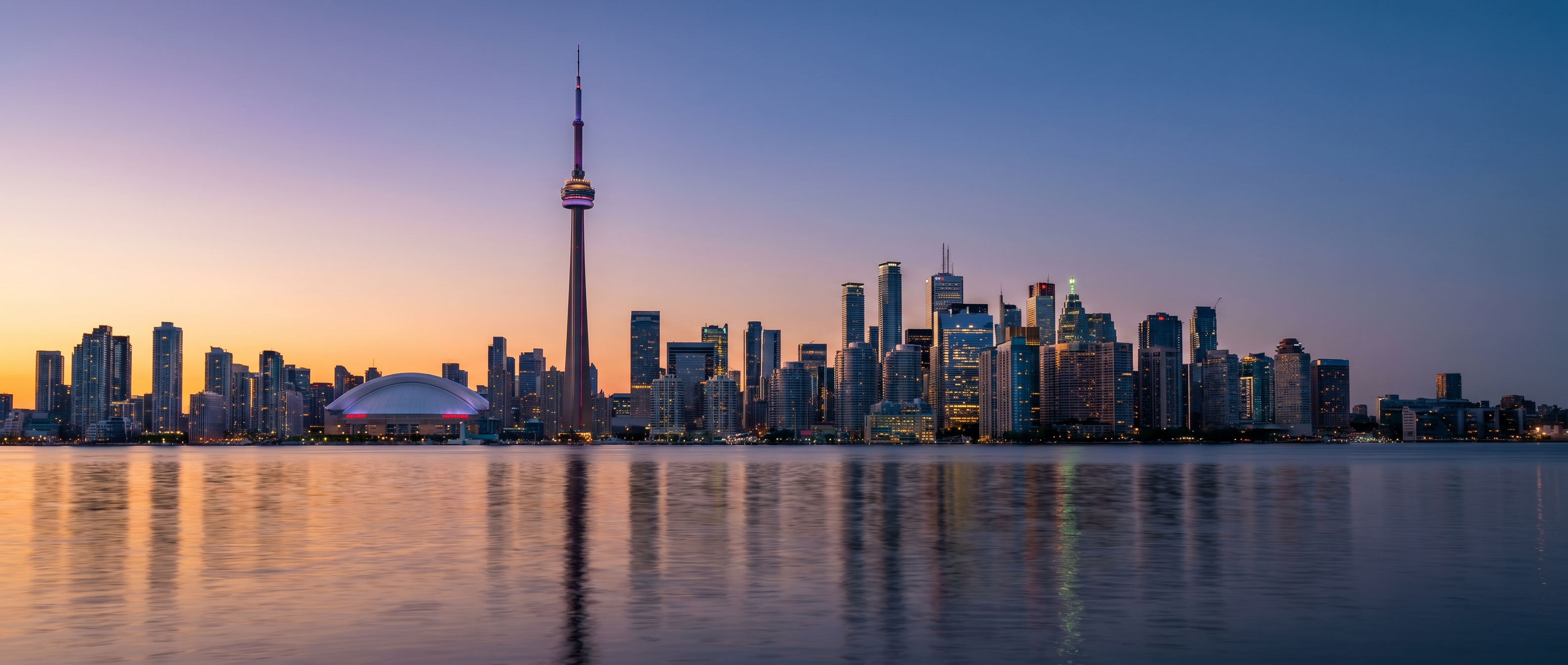 Toronto downtown skyline at dusk with CN Tower, Rogers Centre, and financial district viewed across Lake Ontario